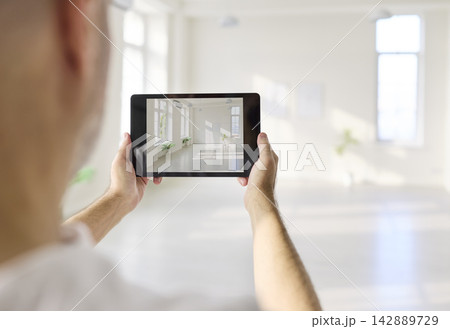 Designer using tablet to photograph bright modern interior room in spacious hall Designer using tablet to photograph bright modern interior room in spacious hall 142889729