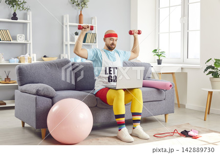 Funny Man Exercising With Dumbbells And Laptop At Home Gym Funny Man Exercising With Dumbbells And Laptop At Home Gym 142889730