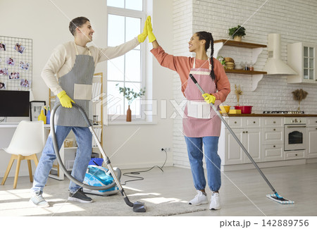 Happy couple doing home cleaning together, vacuuming and mopping in apartment Happy couple doing home cleaning together, vacuuming and mopping in apartment 142889756