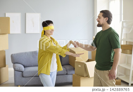 Happy couple moving into new home, man leads blindfolded woman for sweet surprise Happy couple moving into new home, man leads blindfolded woman for sweet surprise 142889765
