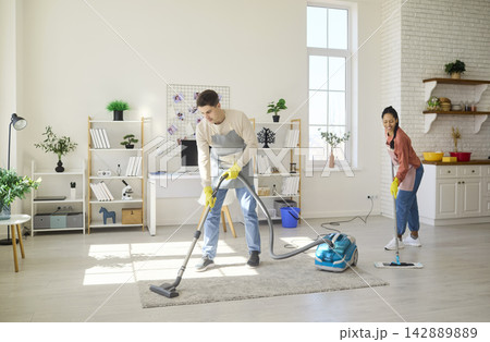 Happy couple cleaning living room together with vacuum and mop, teamwork at home Happy couple cleaning living room together with vacuum and mop, teamwork at home 142889889