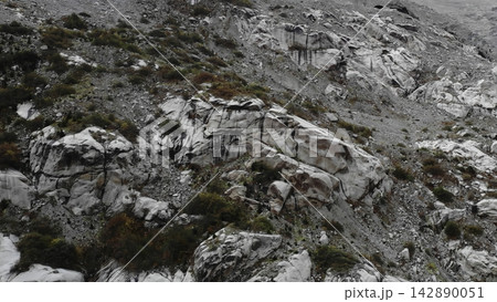 Rugged rocky mountain slope with layered stone and sparse vegetation . Media Rugged rocky mountain slope with layered stone and sparse vegetation . Media 142890051