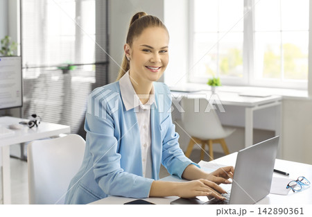 Smiling businesswoman accountant working on laptop in bright modern office interior 142890361