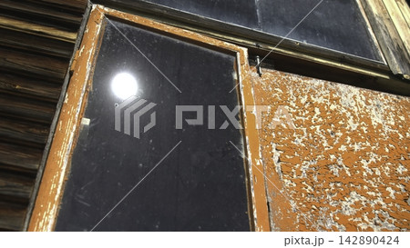 Weathered orange window frame with peeling paint and dark reflective glass Weathered orange window frame with peeling paint and dark reflective glass 142890424