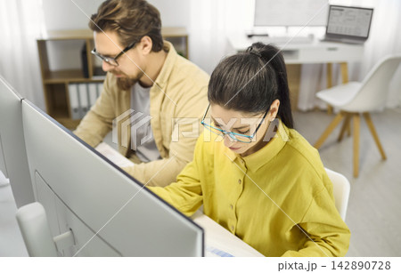 Focused female analyst working on spreadsheets at desktop monitors in office Focused female analyst working on spreadsheets at desktop monitors in office 142890728