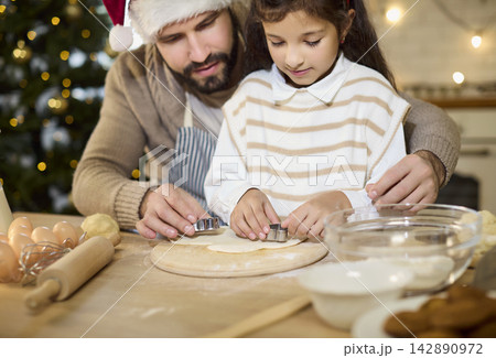 Father guiding daughter cut shapes dough for Christmas cookies in cozy home kitchen Father guiding daughter cut shapes dough for Christmas cookies in cozy home kitchen 142890972