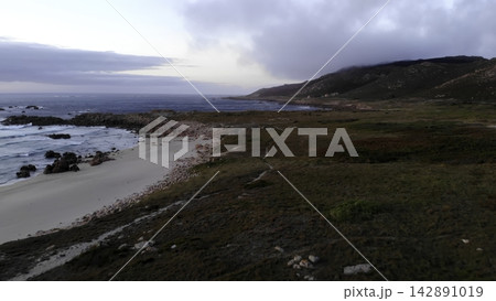 Rugged coastal shoreline with rocky beach and cloudy sky 142891019