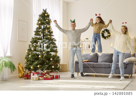 Christmas family dancing with joy, playing near Xmas tree, parents lift child Christmas family dancing with joy, playing near Xmas tree, parents lift child 142891085