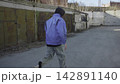 Back view person in blue jacket walking through industrial yard beside metal containers under muted daylight, with person, walking, blue, jacket detail, showing industrial, yard, container, metal 142891140