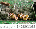炭火の網の上で香ばしく焼かれるイカの姿焼き（海鮮バーベキュー・屋台飯） 142891168
