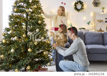 Happy family decorating Christmas tree with lights and baubles in living room Happy family decorating Christmas tree with lights and baubles in living room 142891238