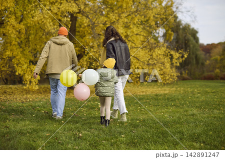 Happy family walking in autumn park with child and balloons, outdoor lifestyle 142891247