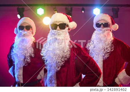 Three Santas dancing at Christmas party under colorful stage lights in shades 142891402