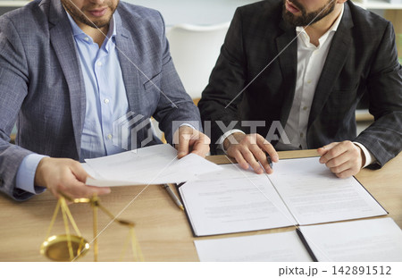 Legal client and lawyer reviewing contract before signing, scales of justice on table 142891512