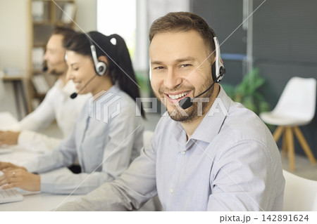 Smiling call center agent with headset helping customers in modern office teamwork Smiling call center agent with headset helping customers in modern office teamwork 142891624