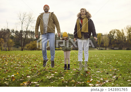 Happy family jumping together in autumn park, parents holding child by hands 142891765