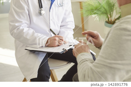 Faceless doctor cardiologist in white coat writing down prescription to old man patient Faceless doctor cardiologist in white coat writing down prescription to old man patient 142891776