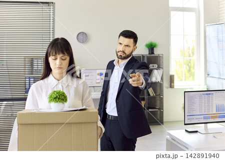 Manager fires employee with box after dismissal in modern office setting Manager fires employee with box after dismissal in modern office setting 142891940