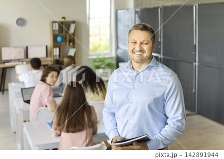 Confident teacher portrait in classroom with students at desks using laptops Confident teacher portrait in classroom with students at desks using laptops 142891944
