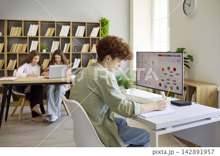 Teen boy studying at desktop with diagram screen in modern classroom setting Teen boy studying at desktop with diagram screen in modern classroom setting 142891957