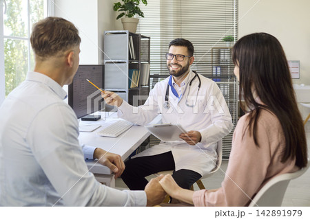 Smiling physician advising couple at clinic desk on fertility and pregnancy Smiling physician advising couple at clinic desk on fertility and pregnancy 142891979