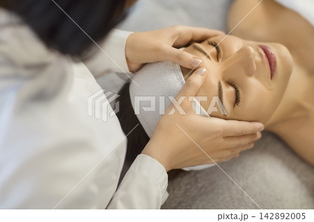 Close up photo of pretty young woman lying with closed eyes and having face or head massage in spa 142892005