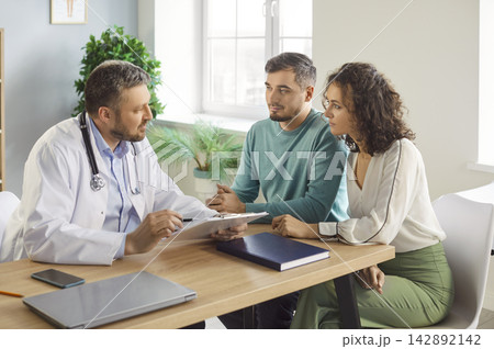 Young couple listening to doctor explaining diagnosis and treatment plan during consultation. Young couple listening to doctor explaining diagnosis and treatment plan during consultation. 142892142