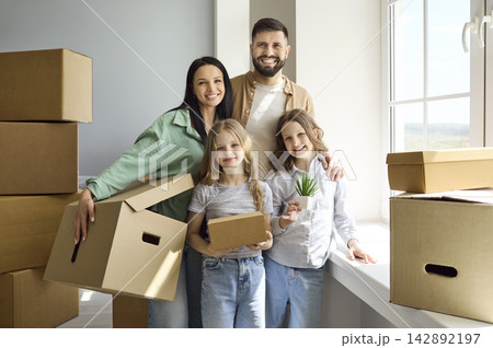 Happy family moving into new home with boxes, parents and children by window Happy family moving into new home with boxes, parents and children by window 142892197