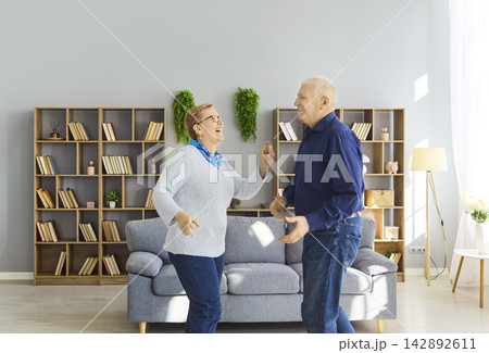 Smiling senior couple dancing at home, celebrating love, wellness and vitality Smiling senior couple dancing at home, celebrating love, wellness and vitality 142892611