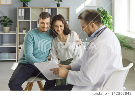 Happy couple hugging while listening to doctor explaining test results and discussing IVF treatment. 142892842