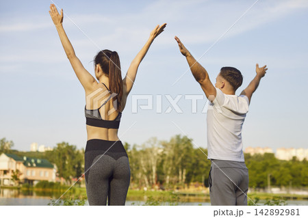 Sporty yogi people actively standing outdoors, raising arms high above head, stretching 142892981