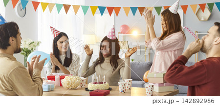 Company of friends gathering together on birthday party, clapping and blowing in party horns 142892986