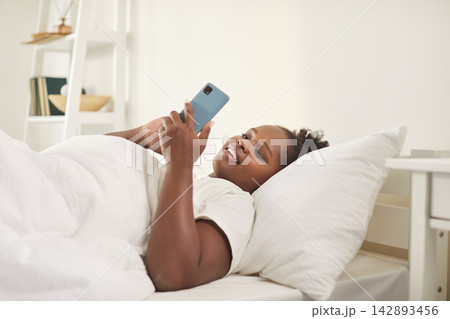 Happy African American Woman Enjoying Leisure On Her Smartphone In Bed At Home 142893456