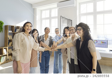 Business women stacking hands in office, celebrating teamwork, unity and success Business women stacking hands in office, celebrating teamwork, unity and success 142893558