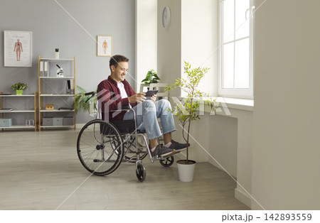 Happy young man in wheelchair using digital tablet, enjoying online communication and entertainment. 142893559
