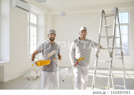 Team of house painters looking at camera holding paint rollers and going to paint the wall 142893561