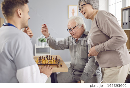 Young nurse man playing chess game with happy smiling senior elderly couple in clinic. 142893602