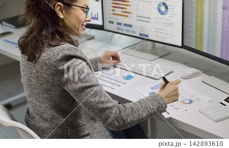 Female accountant analyzing financial data on computer monitors with spreadsheets 142893610