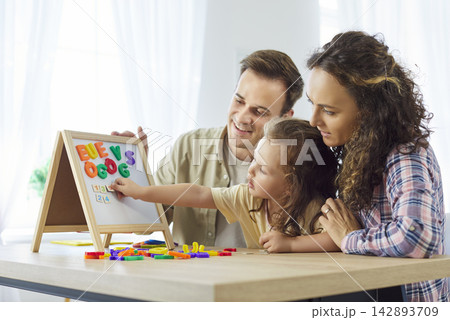 Parents guide daughter learning alphabet on magnetic board at home together 142893709