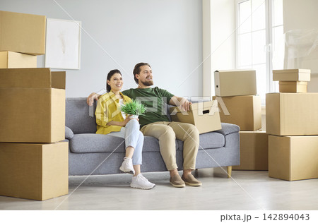 Smiling couple on sofa amid moving boxes, planning and unpacking in new home 142894043