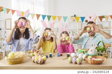 Happy parents with smiling kids having fun putting Easter eggs on eyes together. 142894124