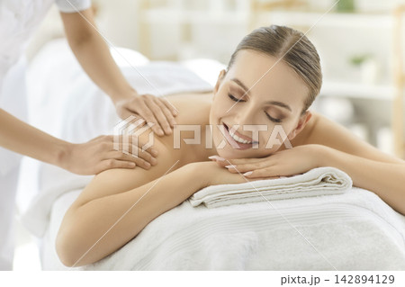 Massage therapist touching back and shoulder of happy woman at spa 142894129