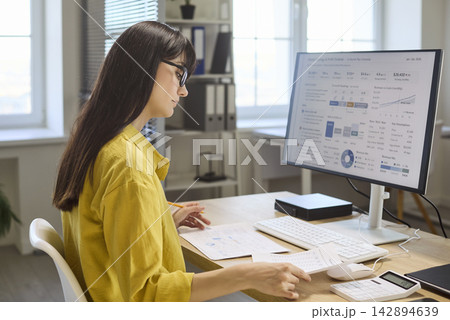 Woman accountant analyzing finance charts at computer with papers and calculator Woman accountant analyzing finance charts at computer with papers and calculator 142894639
