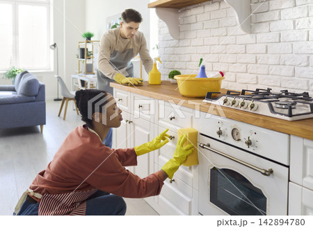 Young couple cleaning kitchen cabinets and oven with sponge, gloves and detergent Young couple cleaning kitchen cabinets and oven with sponge, gloves and detergent 142894780