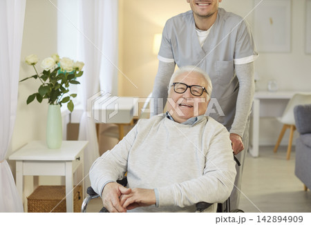 Smiling elderly man in wheelchair enjoying time at home with caregiver offering support and care. 142894909