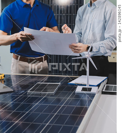 Two Asian engineers wearing hardhats and safety vests discussing solar panel installation and renewable energy project in the office. Two Asian engineers wearing hardhats and safety vests discussing solar panel installation and renewable energy project in the office. 142896145