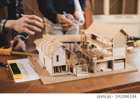 Asian architect and engineer team checking architectural house model using measuring tape on the table at office studio. 142896184