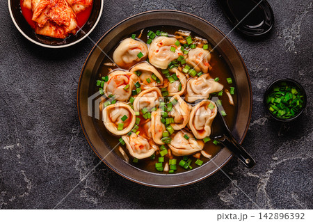 Dumplings served in a bowl with broth and green onions. 142896392