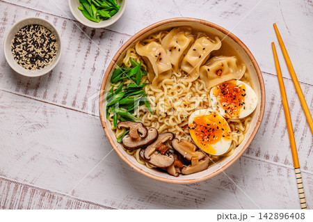 Bowl of noodles with dumplings, egg, and mushrooms on a wooden table Bowl of noodles with dumplings, egg, and mushrooms on a wooden table 142896408