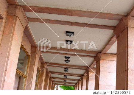 Architectural Symmetry in a Columned Walkway with Stone Pillars and Ceiling Lights Architectural Symmetry in a Columned Walkway with Stone Pillars and Ceiling Lights 142896572